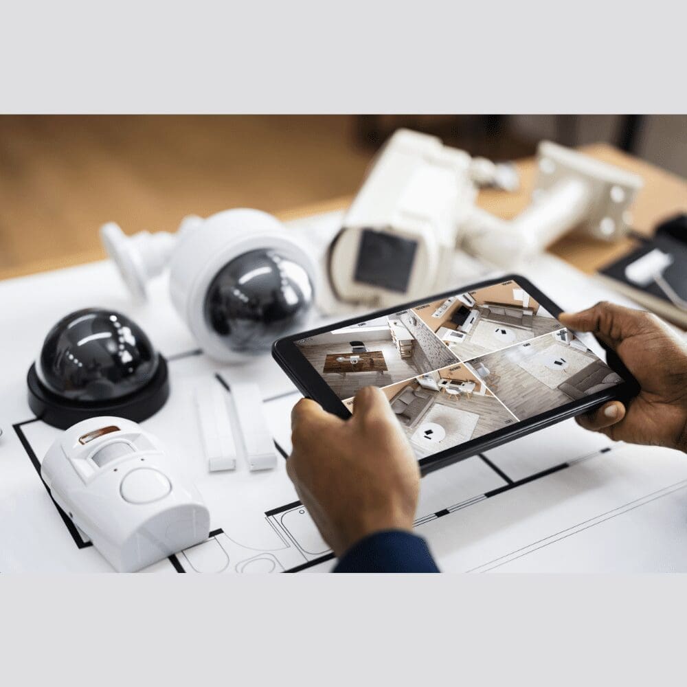 man holding small tablet with four camera views on a table with 5 security cameras on it